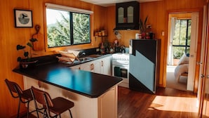 A kitchen with wooden walls, a large window, a refrigerator, and a sink. - Kelp Cabin - intimate, calm and restful (White Beach)