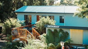 A blue building with a 'GETAWAY' sign, a wooden deck, and lush greenery. - Kelp Cabin - intimate, calm and restful (White Beach)