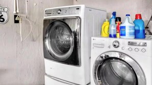 A laundry area with a front-loading washer and dryer, and various cleaning supplies on the dryer.