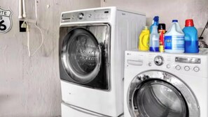 A laundry area with a front-loading washer and dryer, and various cleaning supplies on the dryer.