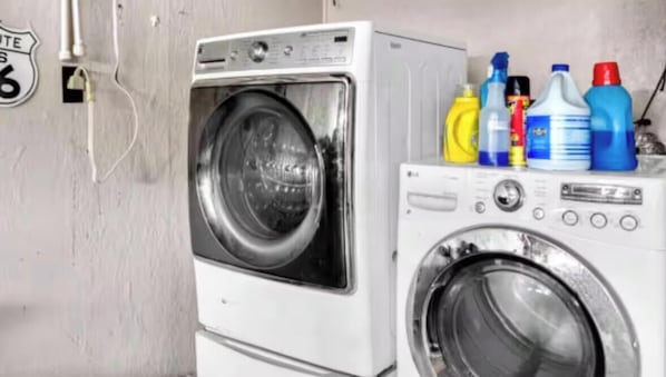 Un área de lavandería con lavadora y secadora de carga frontal, y diversos productos de limpieza sobre la secadora.