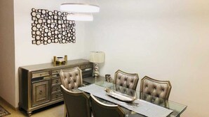 A dining area with a glass table, four upholstered chairs, a dark wooden cabinet, and a decorative wall piece.