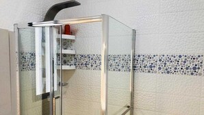 A glass-enclosed shower with a white textured wall and a blue and white mosaic border.