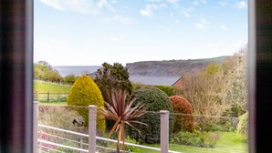 A view from a window overlooking a landscaped garden with various shrubs and a distant view of a hilly landscape. - 4 bedroom accommodation in Runswick Bay (Runswick Bay)