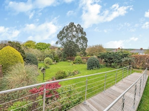 A well-maintained garden with a wooden deck and metal railing, surrounded by various shrubs and trees. - 4 bedroom accommodation in Runswick Bay (Runswick Bay)
