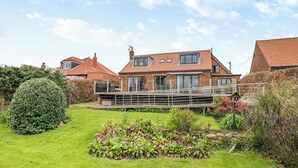 A two-story house with a balcony, surrounded by a well-maintained garden with various plants and a neatly trimmed hedge. - 4 bedroom accommodation in Runswick Bay (Runswick Bay)