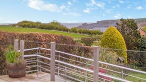 A scenic view of a coastal landscape with a clear sky, a fenced garden area, and a distant cliff. - 4 bedroom accommodation in Runswick Bay (Runswick Bay)