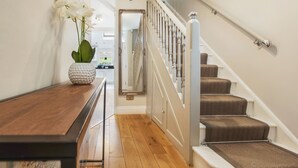 A wooden floor, a white vase with flowers, a mirror, and a staircase with brown carpeted steps. - Luxurious yet cosy Family home (London)