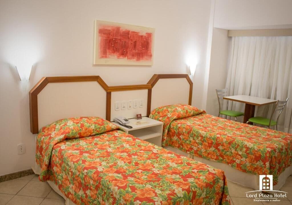 A hotel room with two single beds, a small table, and a chair.