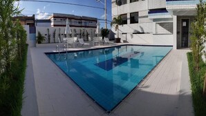 Une piscine extérieure rectangulaire, dotée d’une terrasse carrelée, entourée de chaises longues et de plantes en pot.