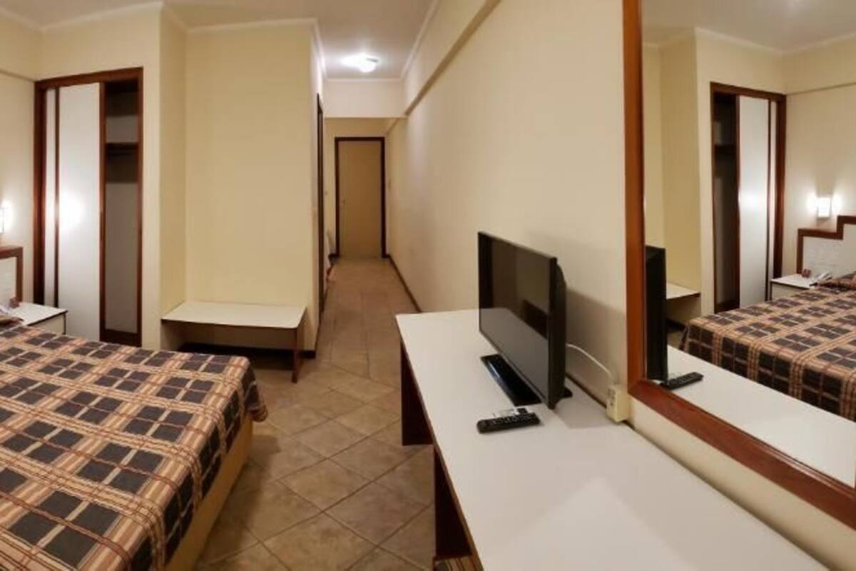 Ein Hotelzimmer mit zwei Betten, einem Fernseher, einem Schreibtisch und einem Spiegel.