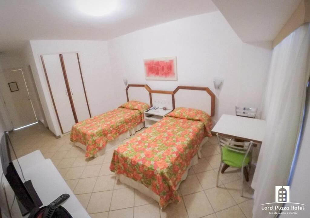 A room with two single beds, a desk, a chair, and a television.