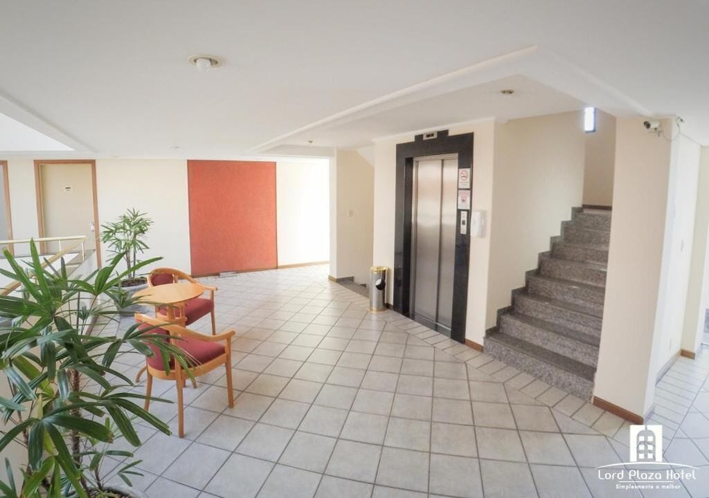 A hotel lobby with a staircase, a trash bin, and a seating area with chairs and a table.