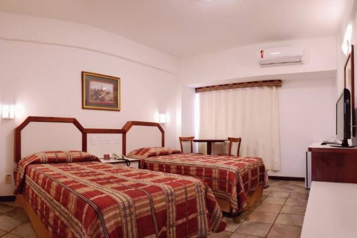 Ein Hotelzimmer mit zwei Betten, einem Schreibtisch, einem Sessel und einem Fernseher.