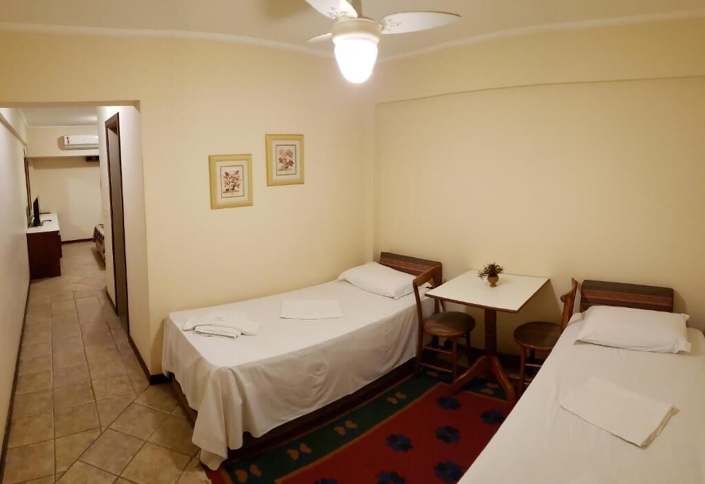A small, clean room with two single beds, a small table, and a chair.