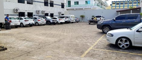 Ein Parkplatz mit mehreren Autos, eine Person in der Nähe eines weißen Autos und Gebäuden im Hintergrund.