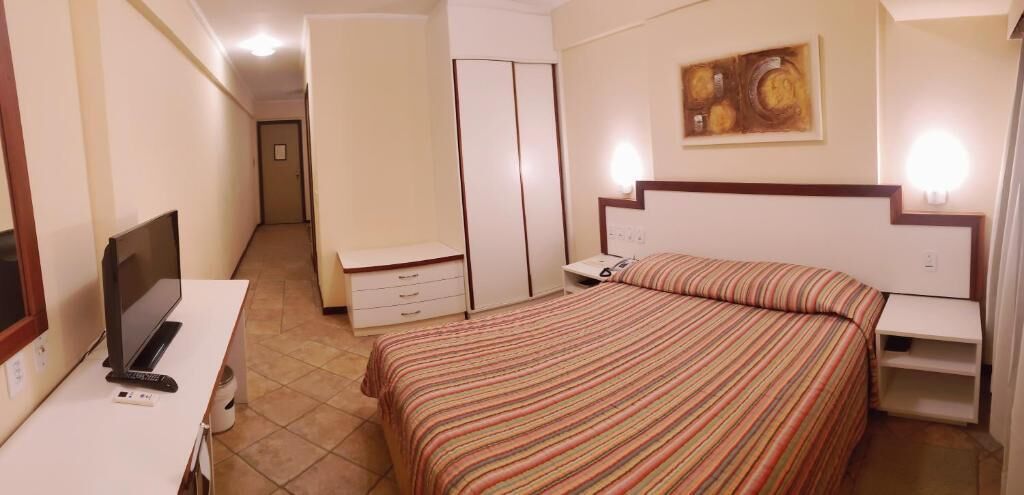 Habitación de hotel con cama, escritorio con computadora, armario y un cuadro en la pared.