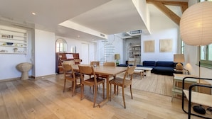 Un vaste espace de vie comprenant une table à manger en bois, des chaises, un canapé et une bibliothèque.