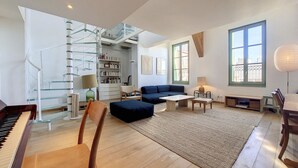 Un salon spacieux avec un piano, un canapé bleu, une chaise en bois, une petite table et une bibliothèque.