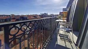 Un balcon donnant sur un paysage urbain, une table avec un vase et une bouteille, et une balustrade.