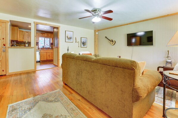 Un soggiorno con un divano, una ventola a soffitto, una TV e una cucina sullo sfondo.