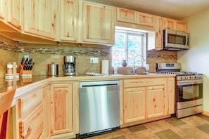 A kitchen with wooden cabinets, a stainless steel dishwasher, a microwave, and a stove. - Fruita Vacation Rental: Walk to Downtown! (Fruita)