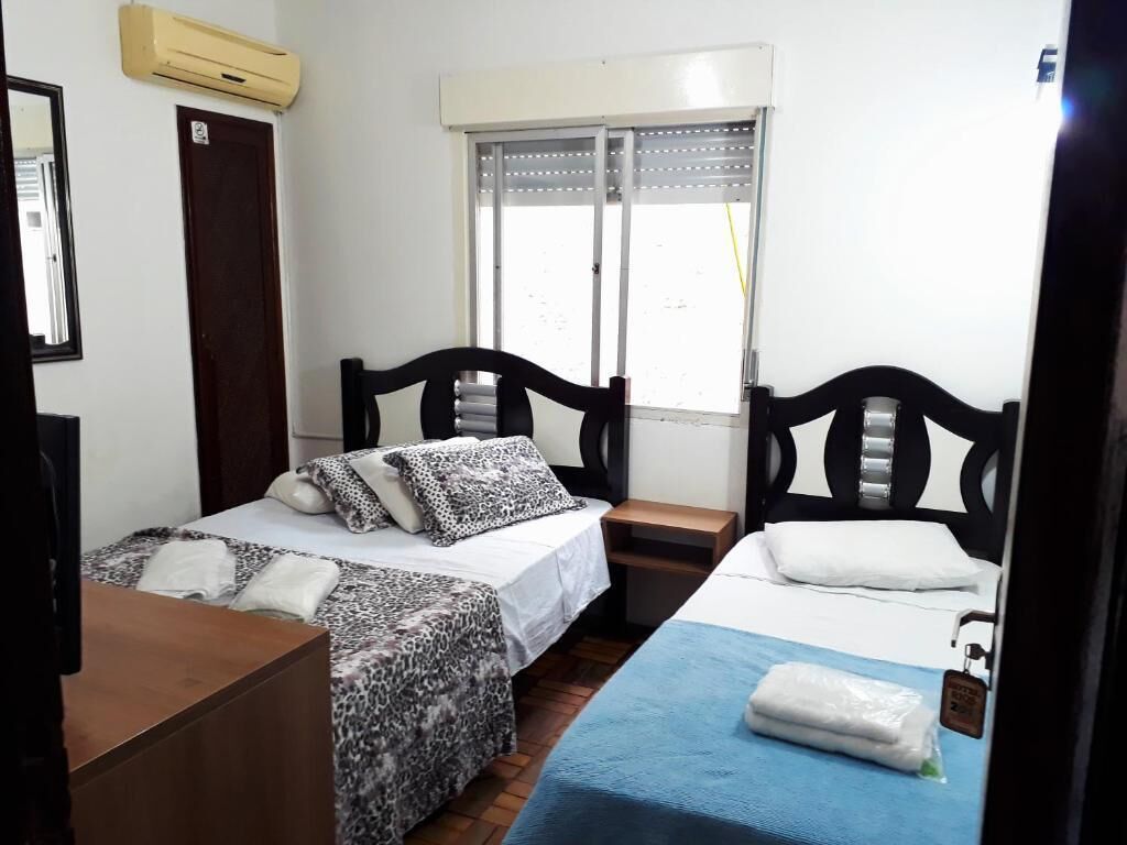 Ein Hotelzimmer mit zwei Betten, einem Holzkopfende, einem Fenster mit Jalousien, einem Nachttisch aus Holz und einem Schreibtisch.