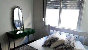 Une chambre à coucher avec un lit, une commode verte, un miroir et une fenêtre avec des stores.