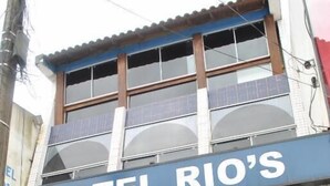 Un hôtel appelé « HOTEL RIO’S », doté d’une grande façade en verre, d’un espace salon bien visible avec des meubles en osier et d’une façade extérieure recouverte de carreaux.