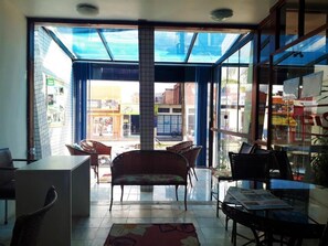A room with a glass door leading to an outdoor area, wicker furniture, and a tiled floor. - Hotel rios  (Jaguarao)