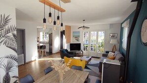 A modern living room with a dining area, a TV, and a large window with a view of the outdoors. - Maison golfe du morbihan (Locmariaquer)