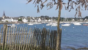 A coastal town with a wooden fence in the foreground, a marina with various boats, and buildings in the background. - Maison golfe du morbihan (Locmariaquer)
