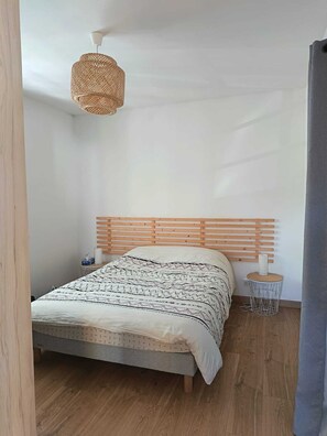 A bedroom with a wooden bed, a woven hanging light, and a bedside table with a lamp. - Maison golfe du morbihan (Locmariaquer)