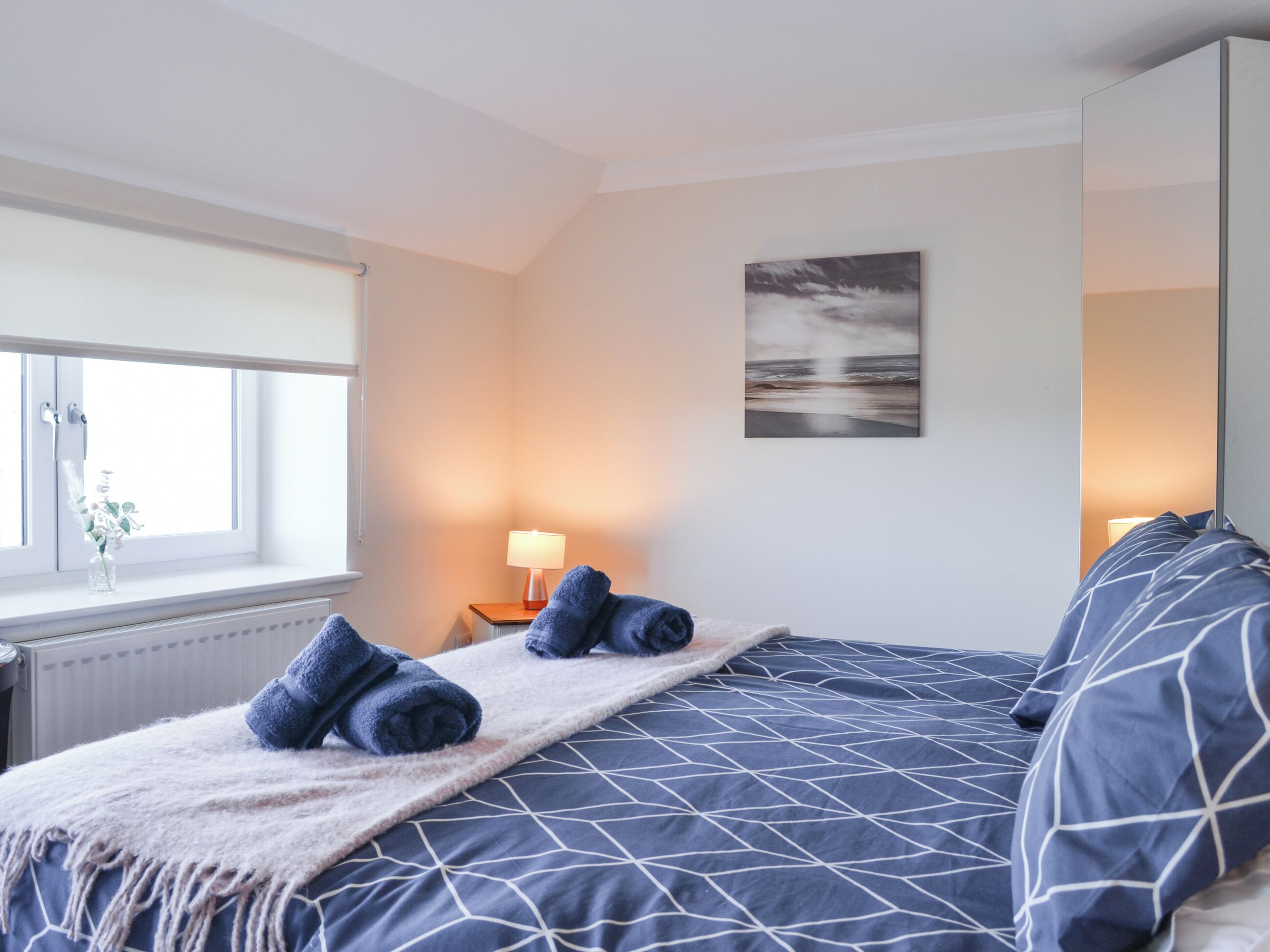 Une chambre à coucher avec un lit, une fenêtre, une lampe et un tableau au mur.