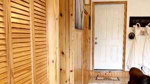 Un couloir en bois avec une porte, un petit tapis et un fauteuil en cuir marron.