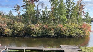Une zone herbeuse avec une jetée en bois qui s’avance sur un lac, le tout entouré d’arbres aux feuilles d’automne.