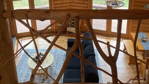 Interior de una cabaña de madera con techo inclinado, dos tragaluces, un ventilador de techo y vistas al exterior a través de las ventanas.