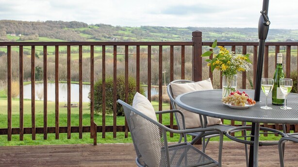 A deck with a table set for two, overlooking a scenic landscape. - Greenfields - UK43269 (Upottery, near Honiton)