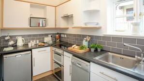 A modern kitchen with white cabinets, a built-in oven, a dishwasher, and a stainless steel sink. - Greenfields - UK43269 (Upottery, near Honiton)