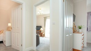A hotel room with a bed, bedside table, lamp, and a view of the living area. - Greenfields - UK43269 (Upottery, near Honiton)