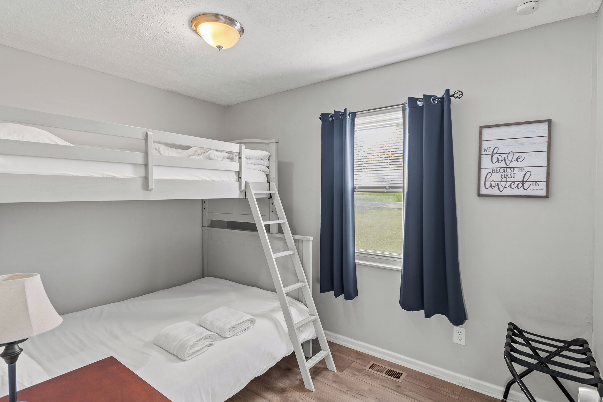 A bunk bed room with a ladder, a window with curtains, a wall-mounted light fixture, and a framed quote on the wall.
