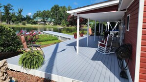 A covered deck with outdoor seating, a pond, and a view of a lake and buildings in the background. - Island Trail's Sunset Cottage on Beautiful Lake Murray - Now with King Size bed! (Chapin)