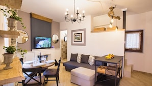 Un salon moderne comprenant un canapé, un pouf, une table à manger et des chaises. On y trouve également un téléviseur, un lustre et un miroir fixé au mur.