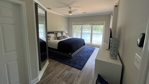 Un dormitorio con cama, ventilador de techo, ventana grande y vista a una masa de agua.
