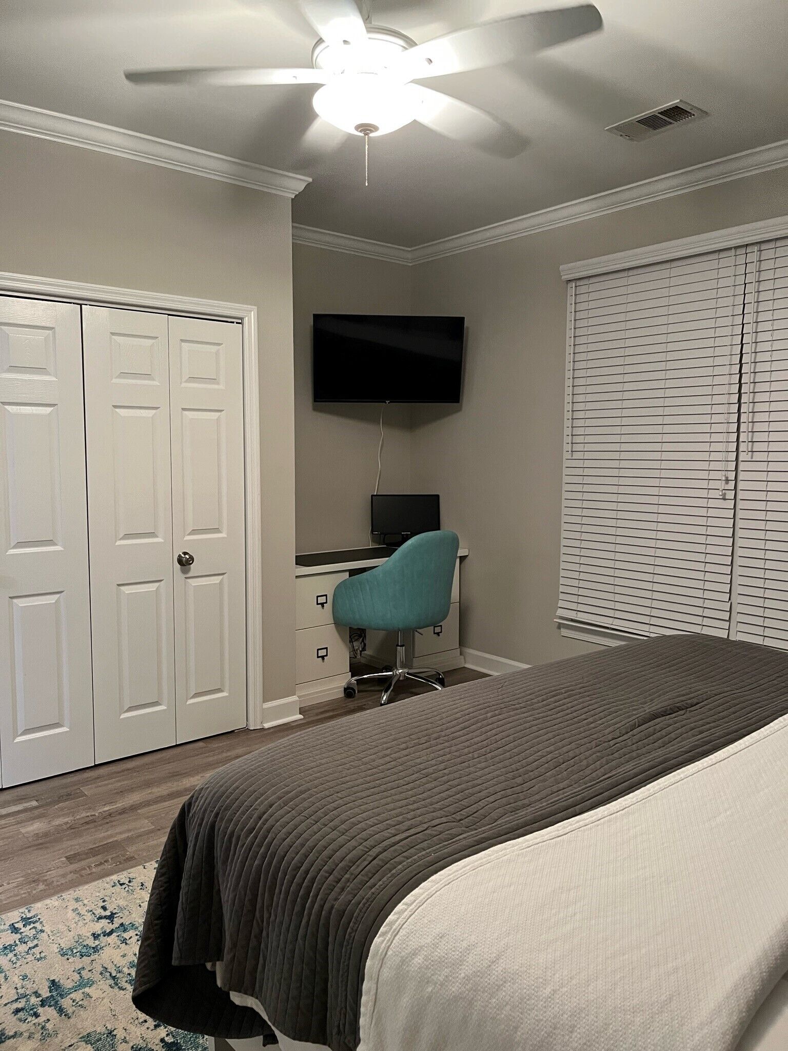 Una camera da letto con un letto, una scrivania con una sedia, una ventola a soffitto, una televisione e un armadio.