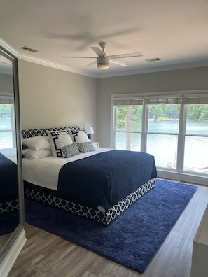 A bedroom with a large bed, a ceiling fan, and a view of a lake through large windows. - Direct Lake-Luxury Home w/ Dock Access – Reynolds, Lake Oconee- Near The Masters (Greensboro)