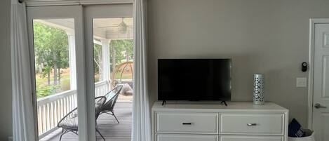 A room with a sliding glass door leading to an outdoor patio, a white dresser with drawers, a flat-screen TV on top, and a small decorative vase.