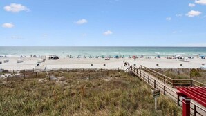 A beach with a wooden walkway leading to the water, a lifeguard tower, and beach umbrellas.