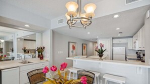 A modern kitchen with white cabinetry, a central island, and a dining area with wicker chairs and a glass table.