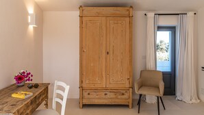 A room with a wooden wardrobe, a white chair, a wooden table with a book and flowers, and a window with curtains. - Dimora Biancarancio - Epoca Collection (Ostuni)